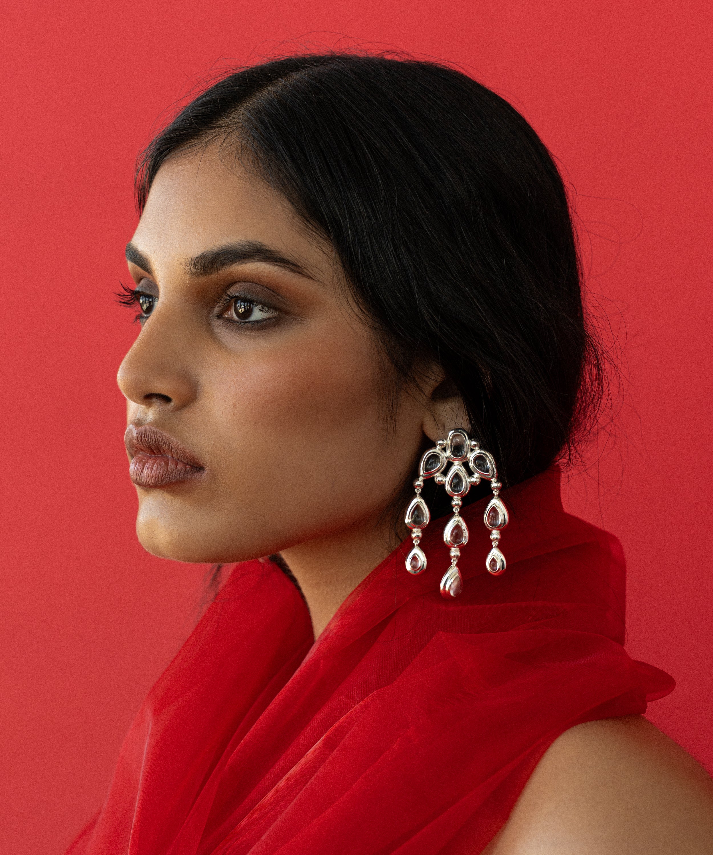 Woman wearing a red outfit with a large mountain and moon earring against a red background
