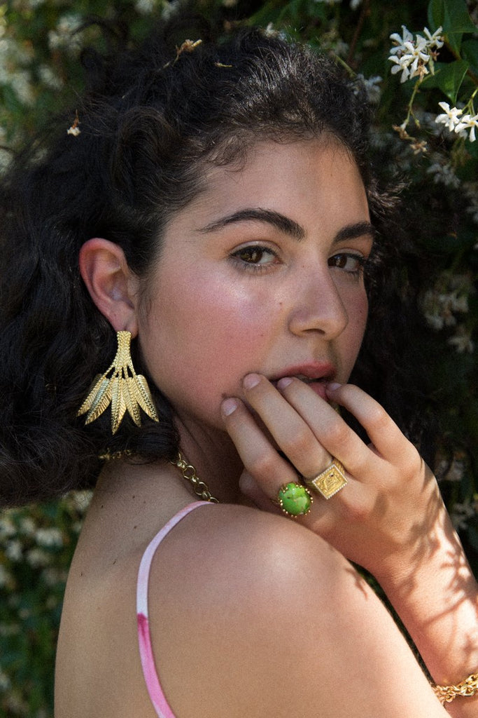 Model wearing Gold BIANCA Cocktail Ring with oval GREEN MOJAVE TURQUOISE, Gold SIGNET Ring and Ravella Palm Tree Statement Earrings by Mountain and Moon Jewellery